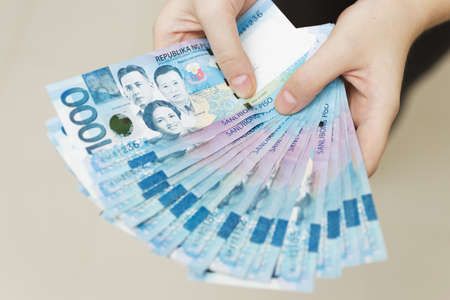 126294208-hands-holding-salary-or-payment-bundle-of-cash-of-one-thousand-philippines-peso-as-if-being-rich.jpg